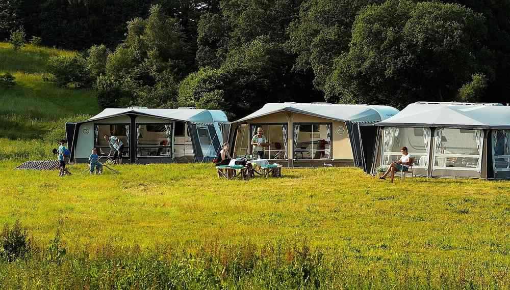 Trois caravanes avec auvents déployés stationnées dans un camping en herbe verte