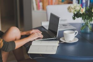 Une femme travaille sur ordinateur, boisson chaude et fleurs à côté