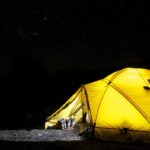 Tente jaune éclairée sous un ciel étoilé nocturne