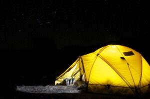 Tente jaune éclairée sous un ciel étoilé nocturne