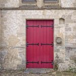 Porte rouge à panneaux encadrée de pierre ancienne sol en pavés