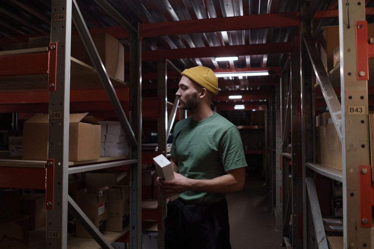 Homme inspecte des boîtes dans un entrepôt avec des étagères métalliques