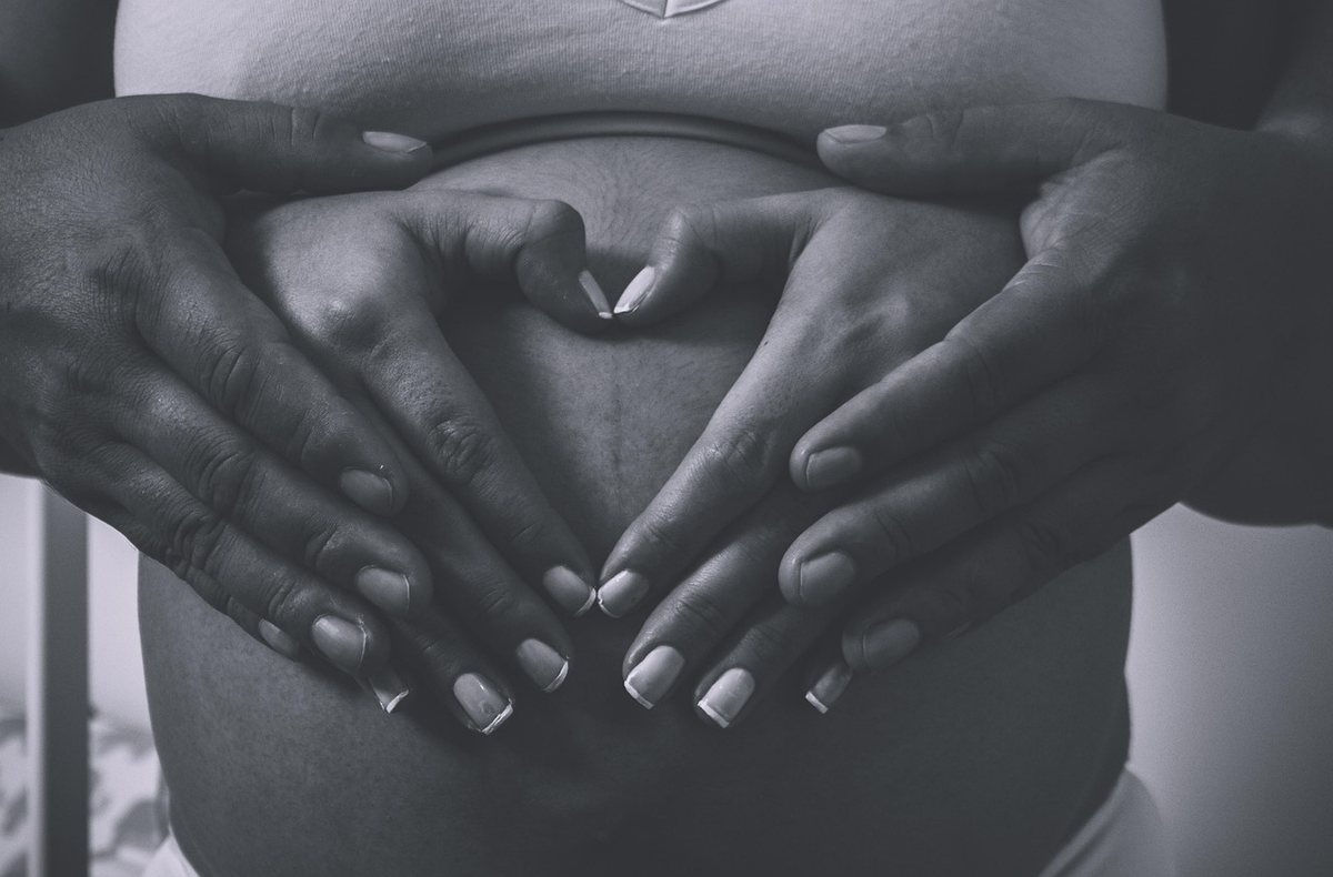 Mains formant un cœur sur le ventre arrondi d'une femme enceinte