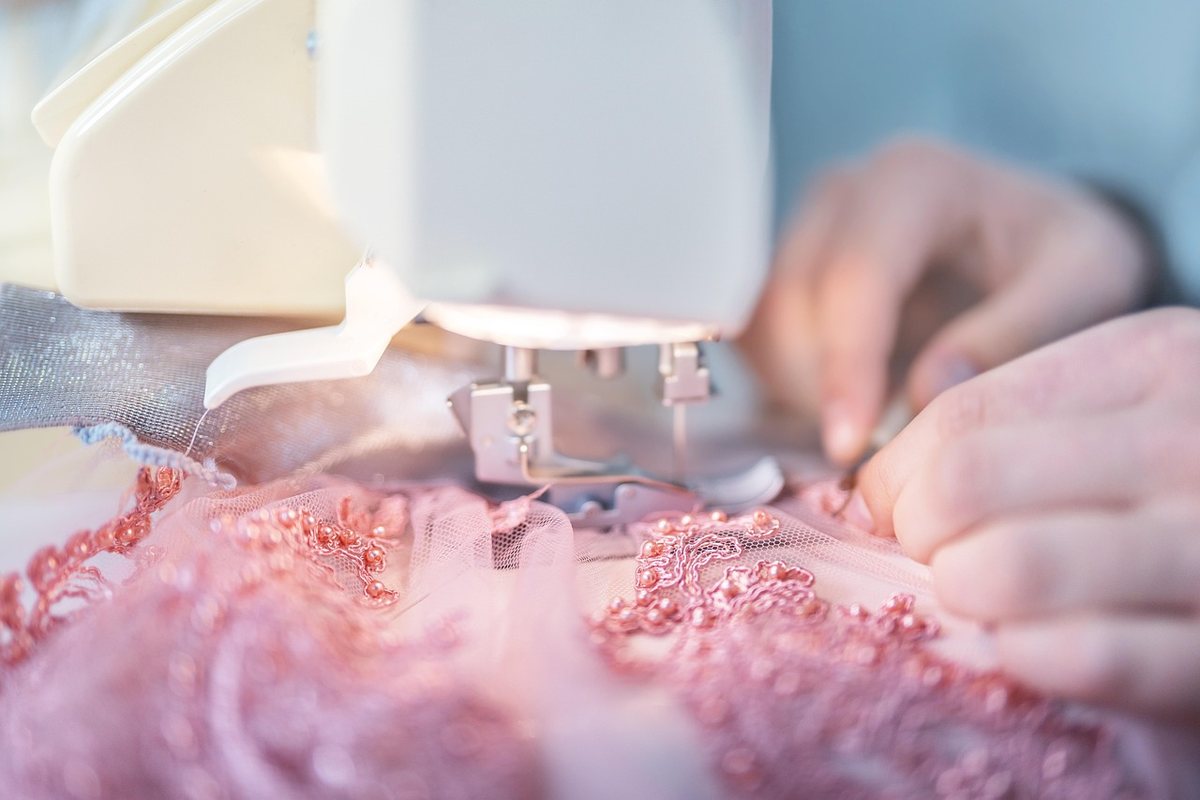 Une main guide le tissu rose sous l'aiguille d'une machine à coudre