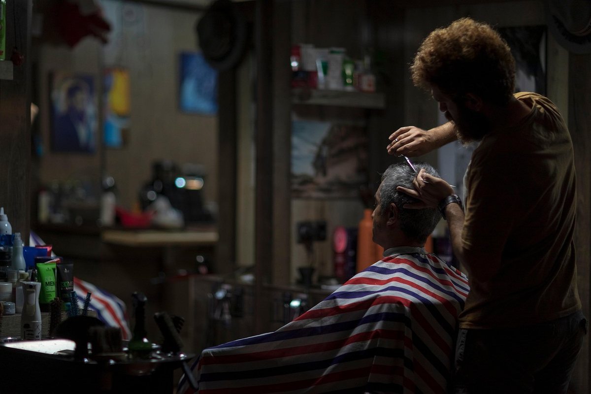 Coiffeur coupe cheveux d'un client dans un salon sombre Coiffeur coupe cheveux d'un client dans un salon sombre